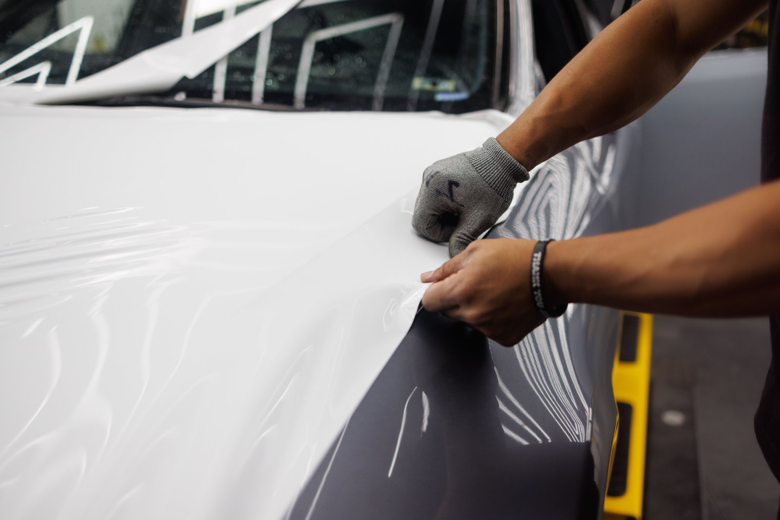 Gros plan sur les mains d'un poseur ajustant un film PPF transparent sur une carrosserie