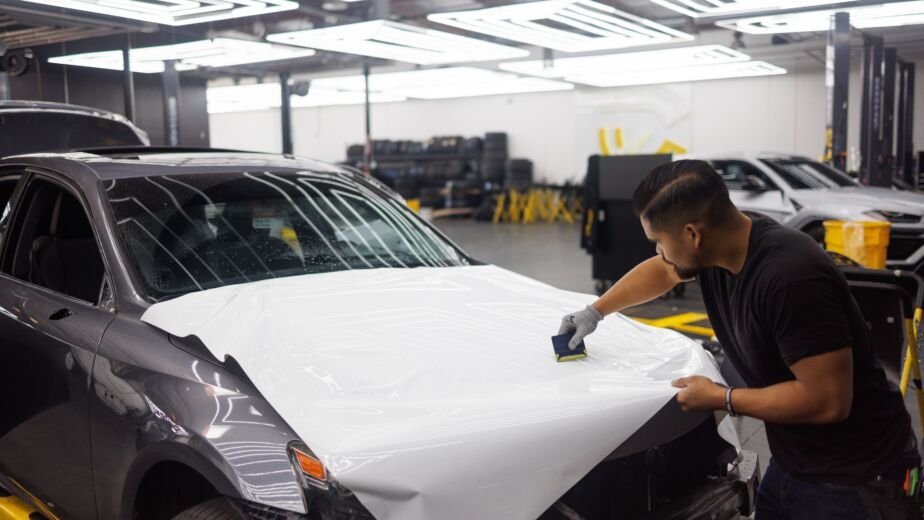 Technicien posant un film PPF transparent sur le capot d un vehicule en atelier