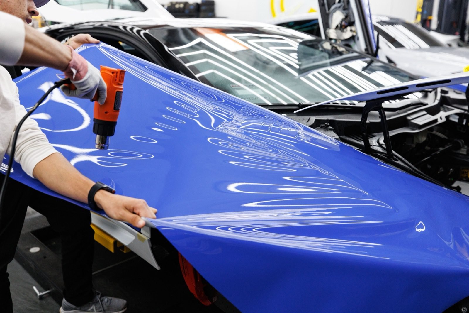 Pose d'un film de protection PPF transparent sur le capot d'une voiture en atelier