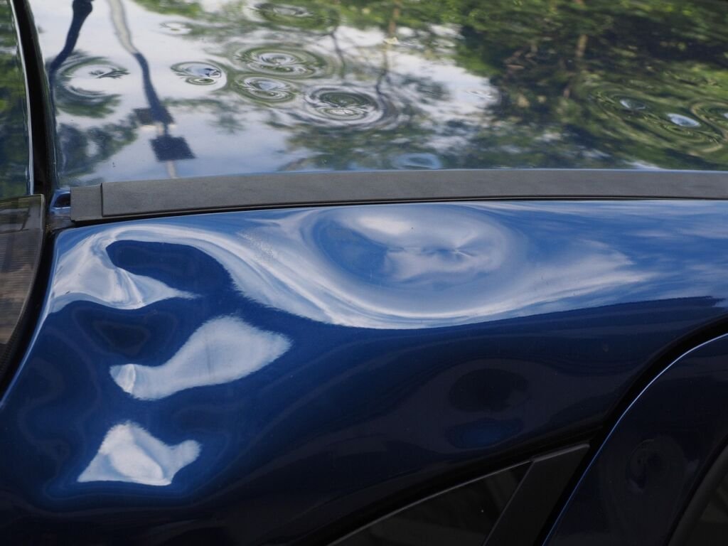 Gros plan sur les bosses de grêle d'une aile de voiture dont la peinture est restée intacte